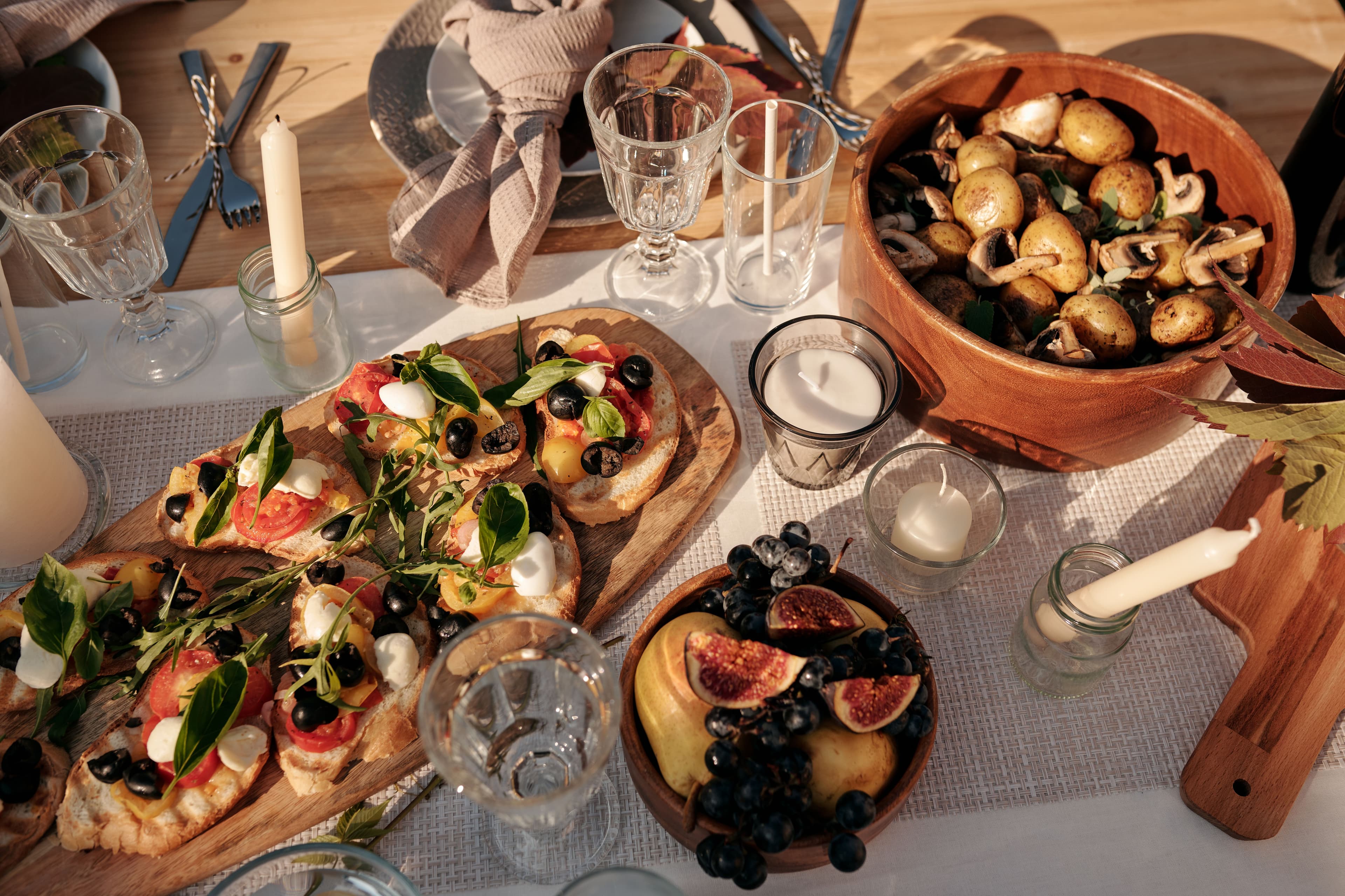 The middle of a breakfast table with a loaf on a board, butter, a jug of water and a bowl of figs