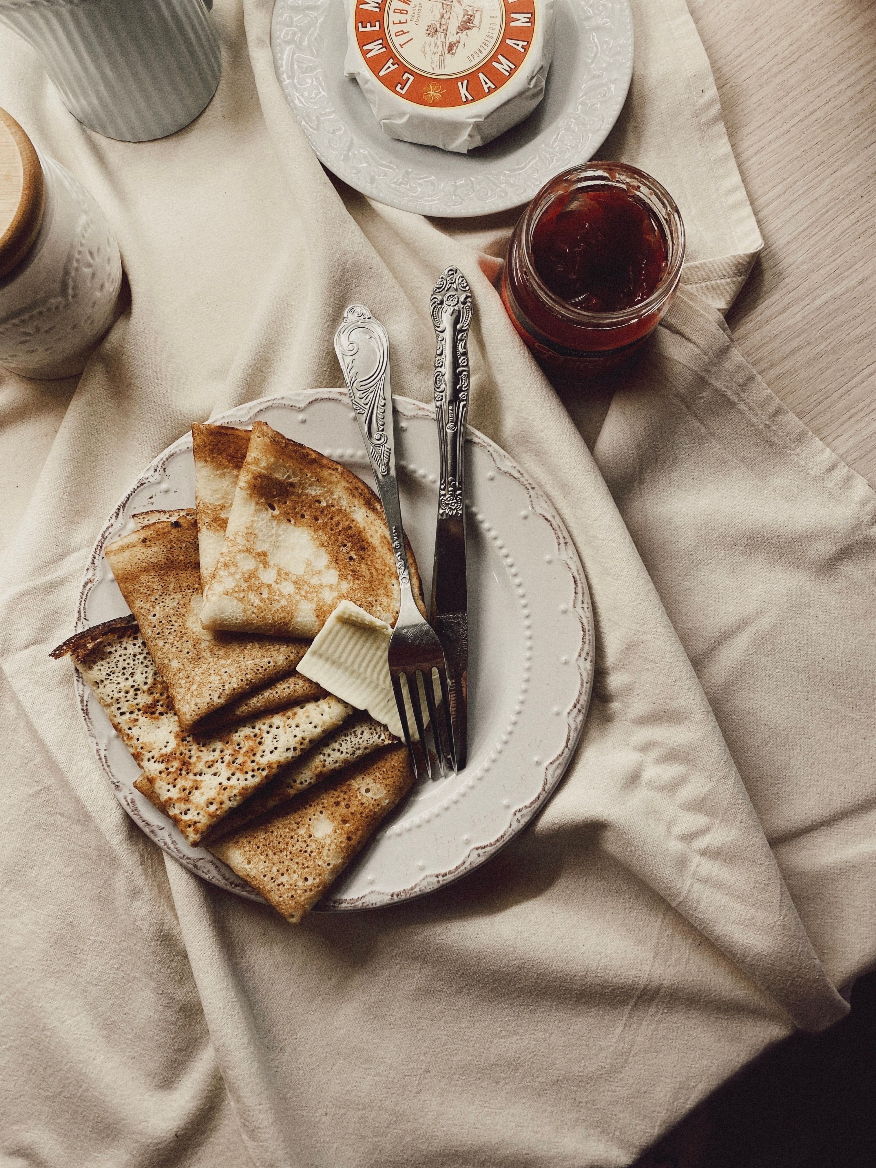 A jar of jam with a spoon standing in it, and butter on a dish with its own knife
