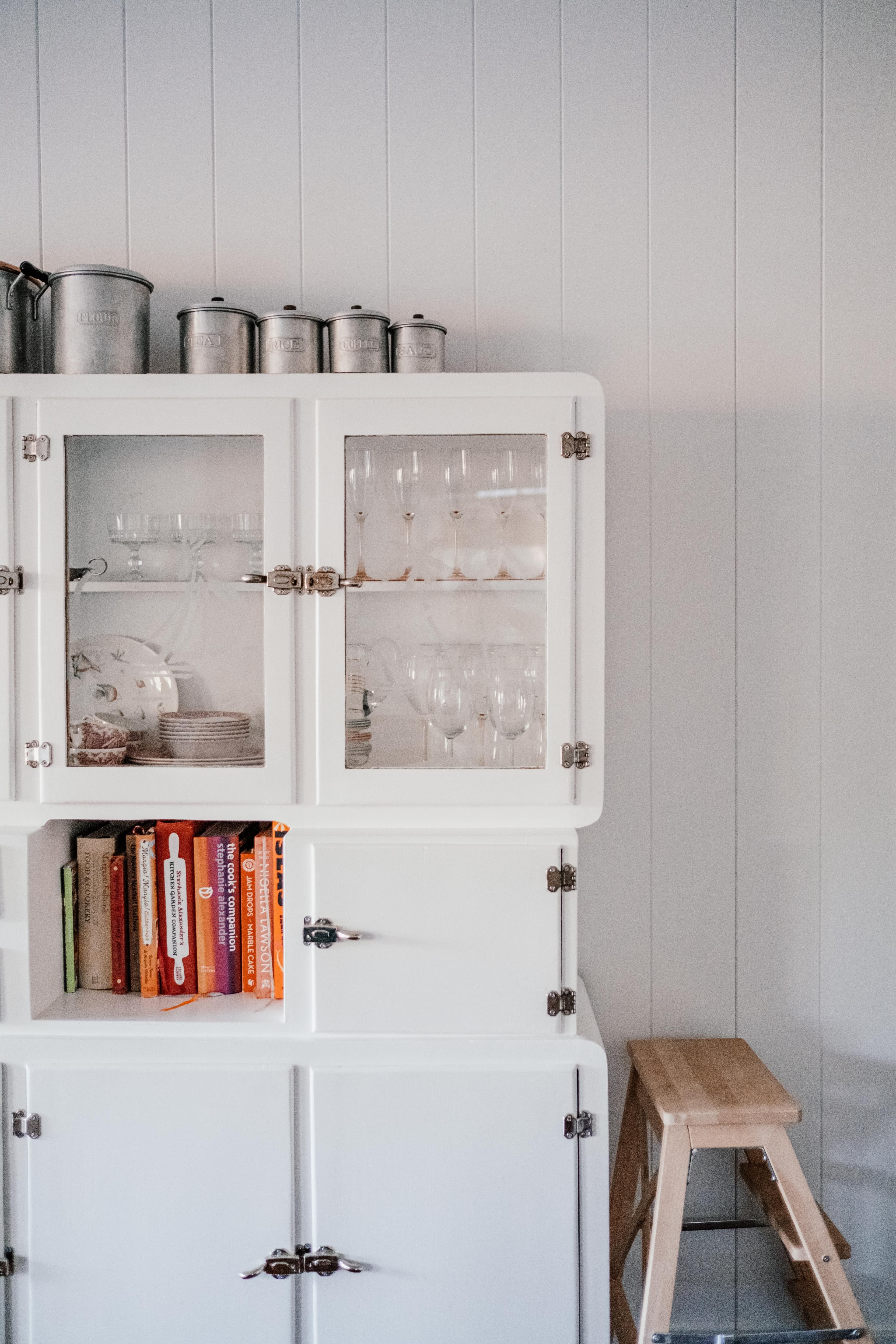 An open cupboard holding tissue-wrapped glasses, folded linen and a felt-lined case of silver