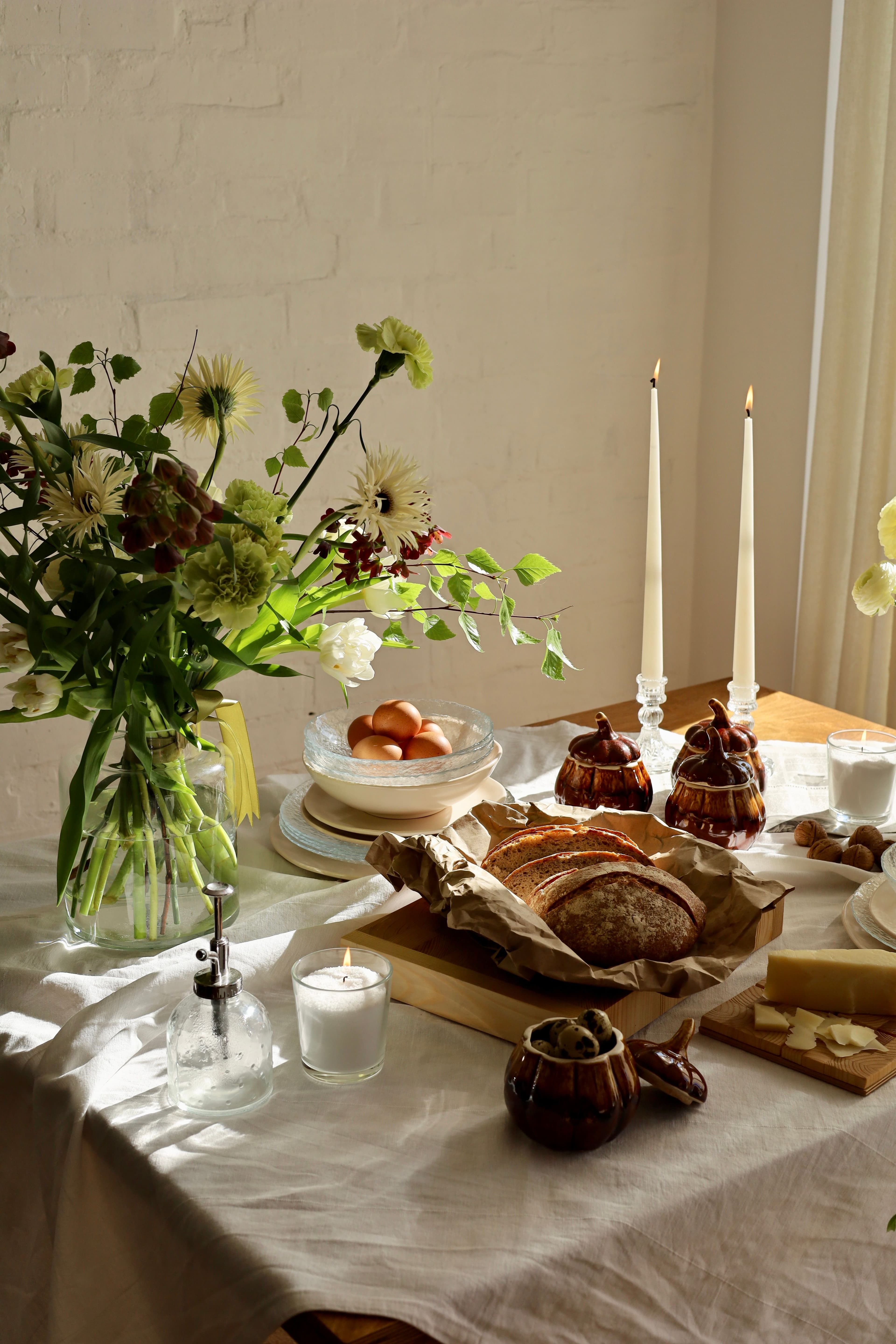 A table laid for two on an ordinary evening, with a heavy water glass, linen napkins and an unlit candle in window light