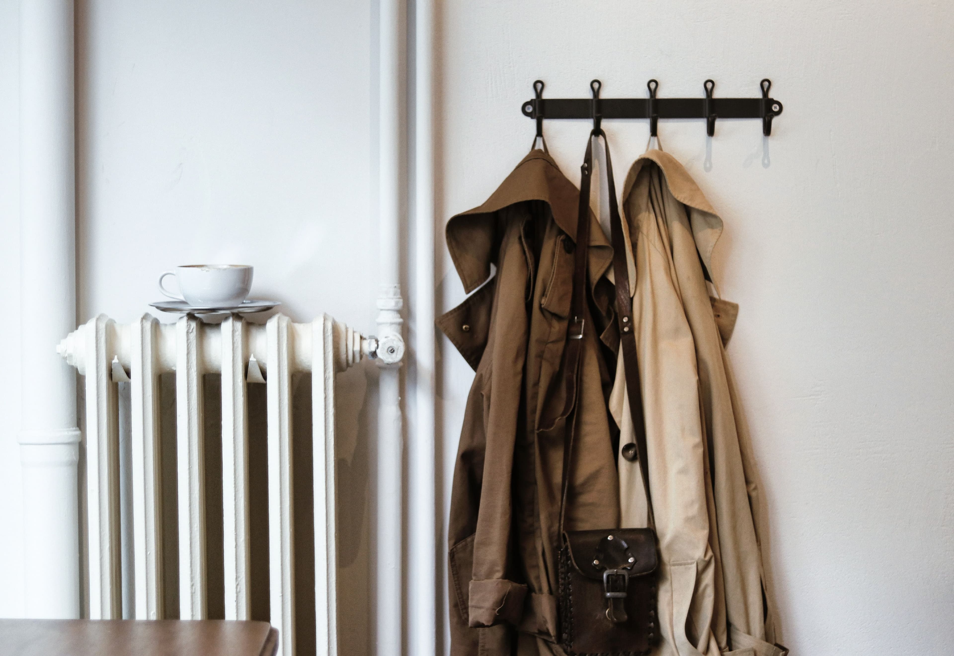 Coats on hooks in a hallway and a hand resting on a door latch