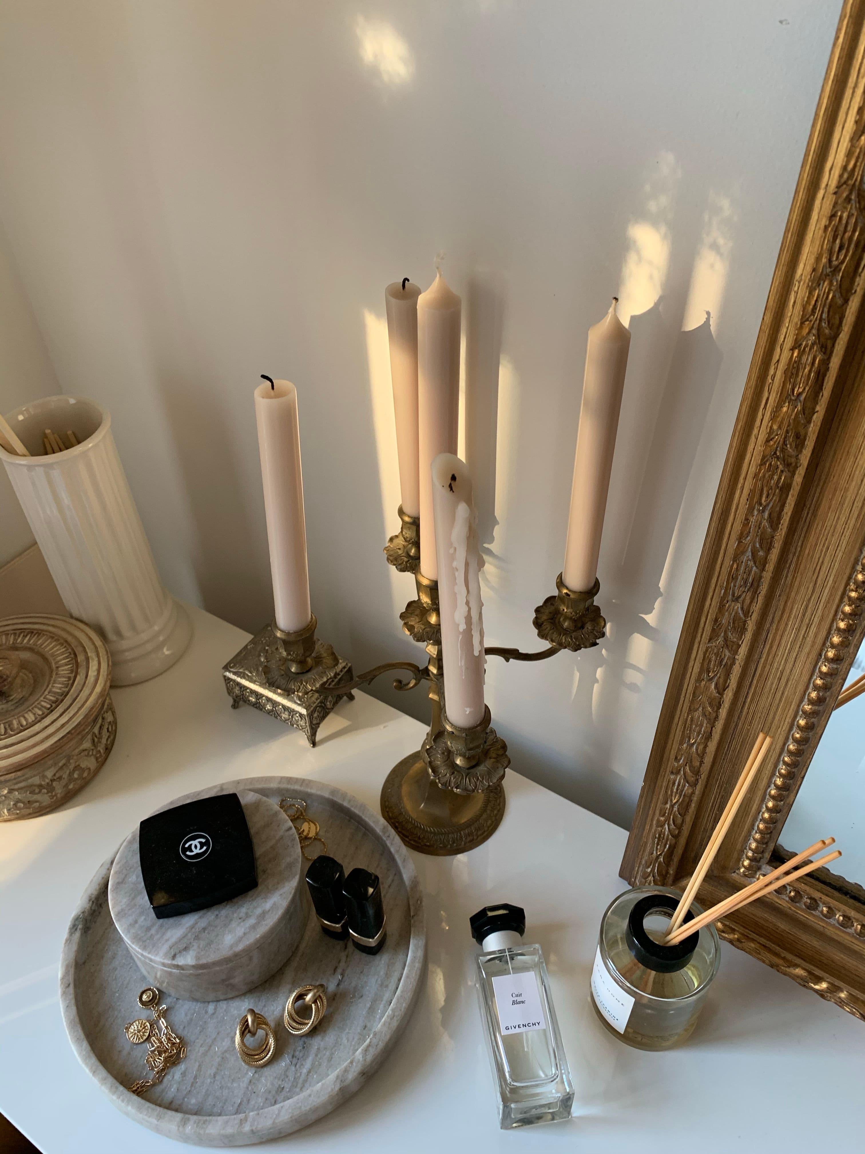 A dressing table by a window in natural light, with a hairbrush, hand mirror, perfume bottle and lipstick on a linen-covered tray