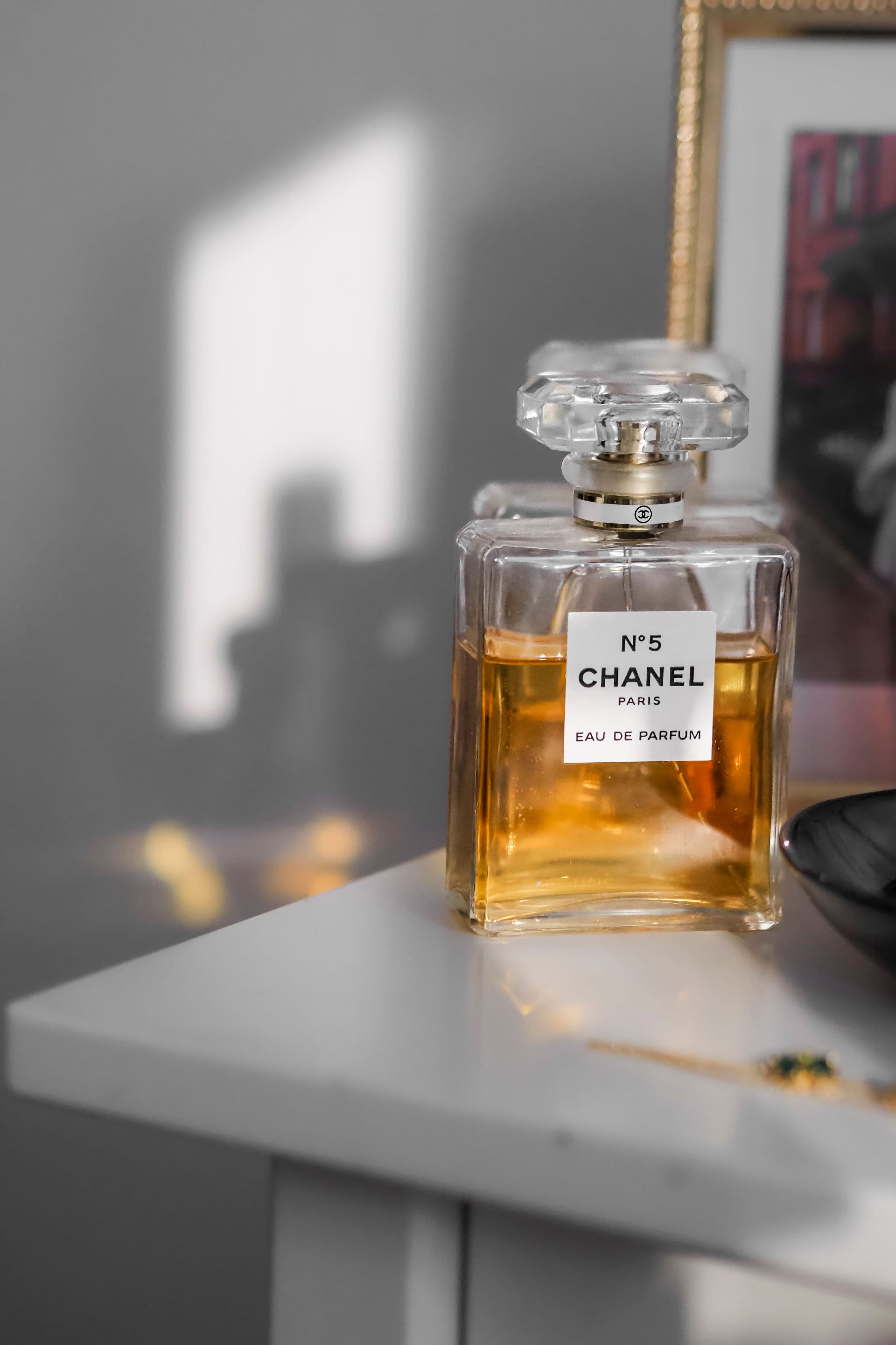 A glass perfume bottle with an atomizer on a dressing table in window light