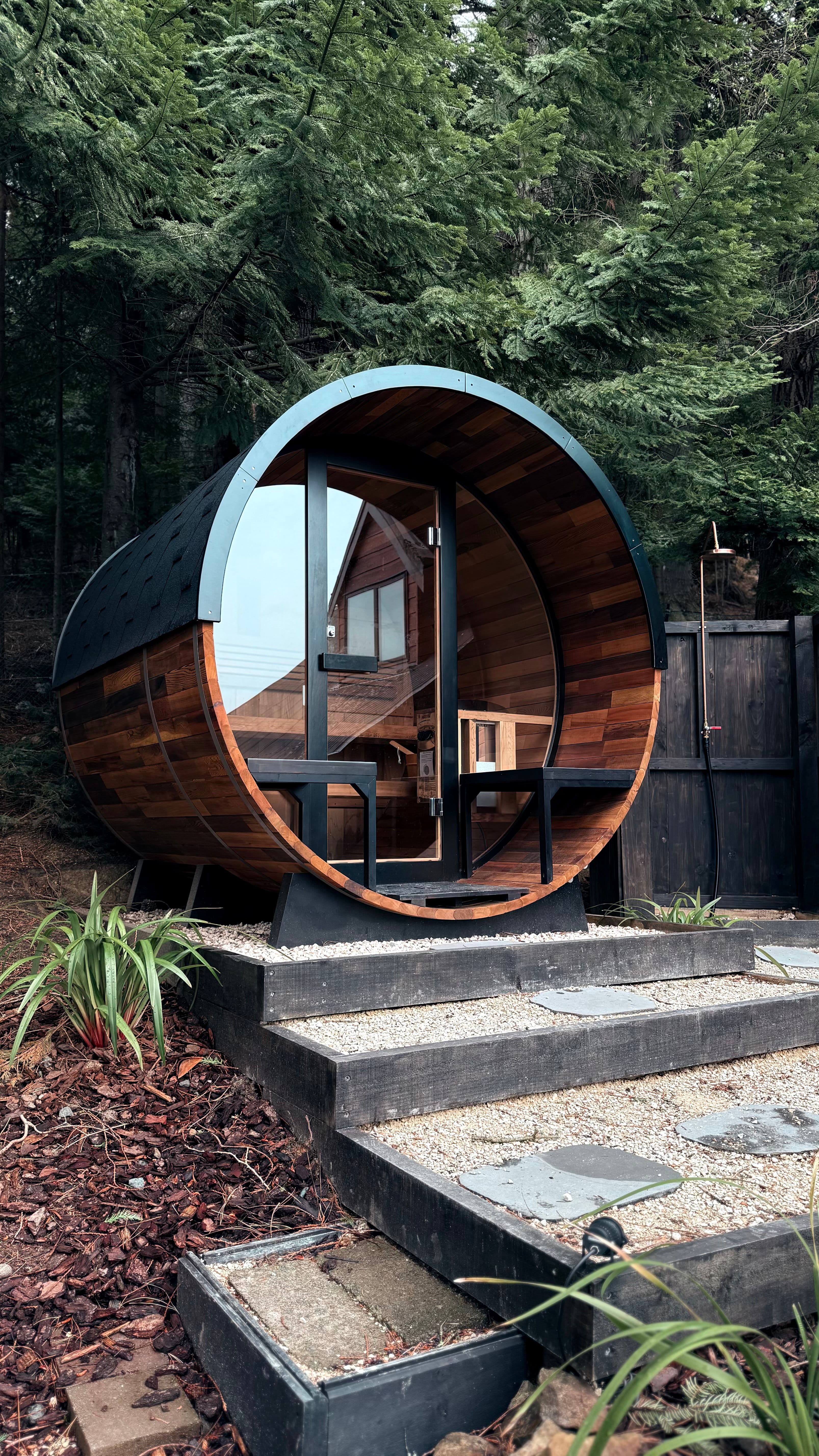 A freestanding timber sauna in a garden, seen from outside in early evening light