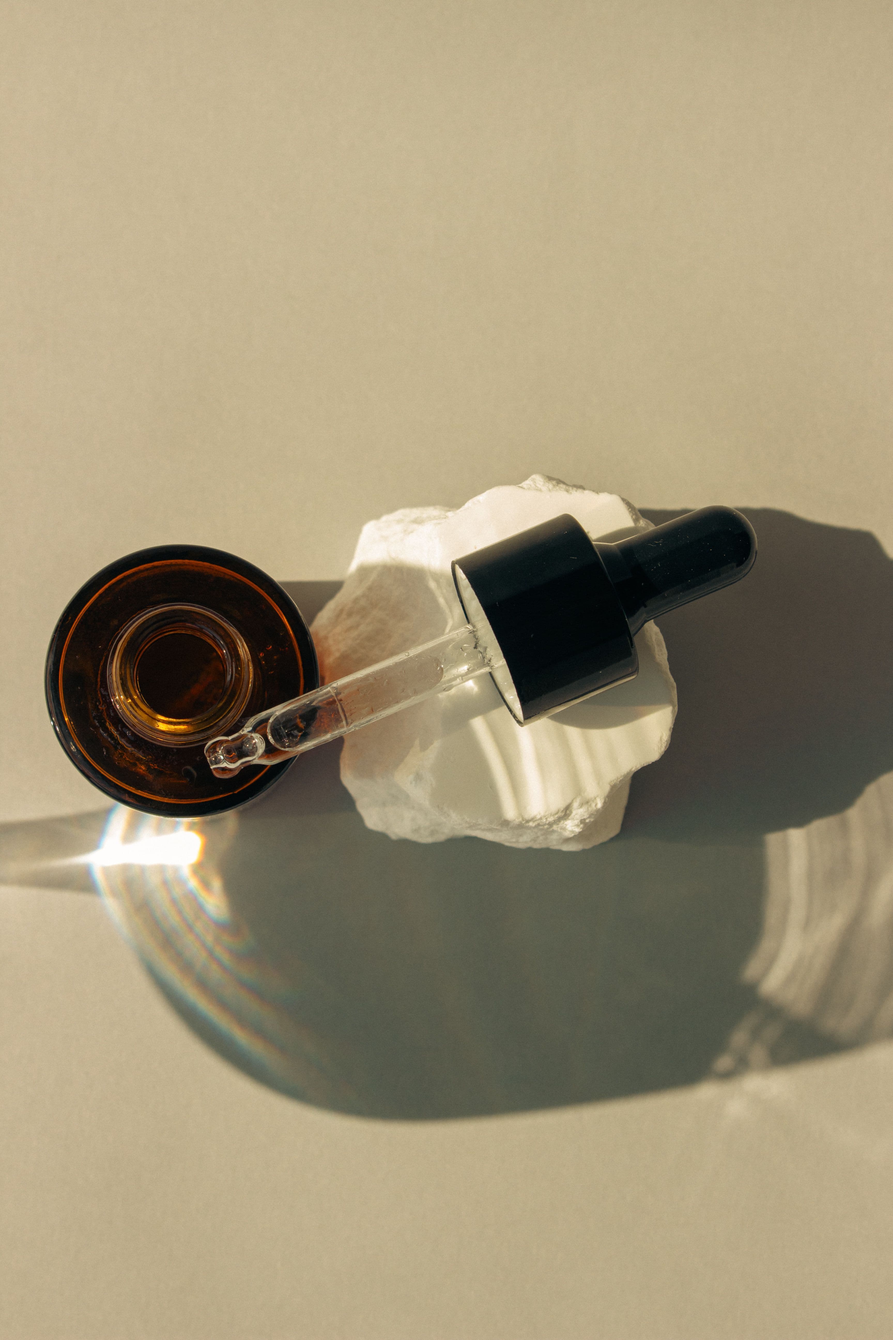A small bottle of cuticle oil beside a glass nail file and a pair of nail clippers on a linen cloth