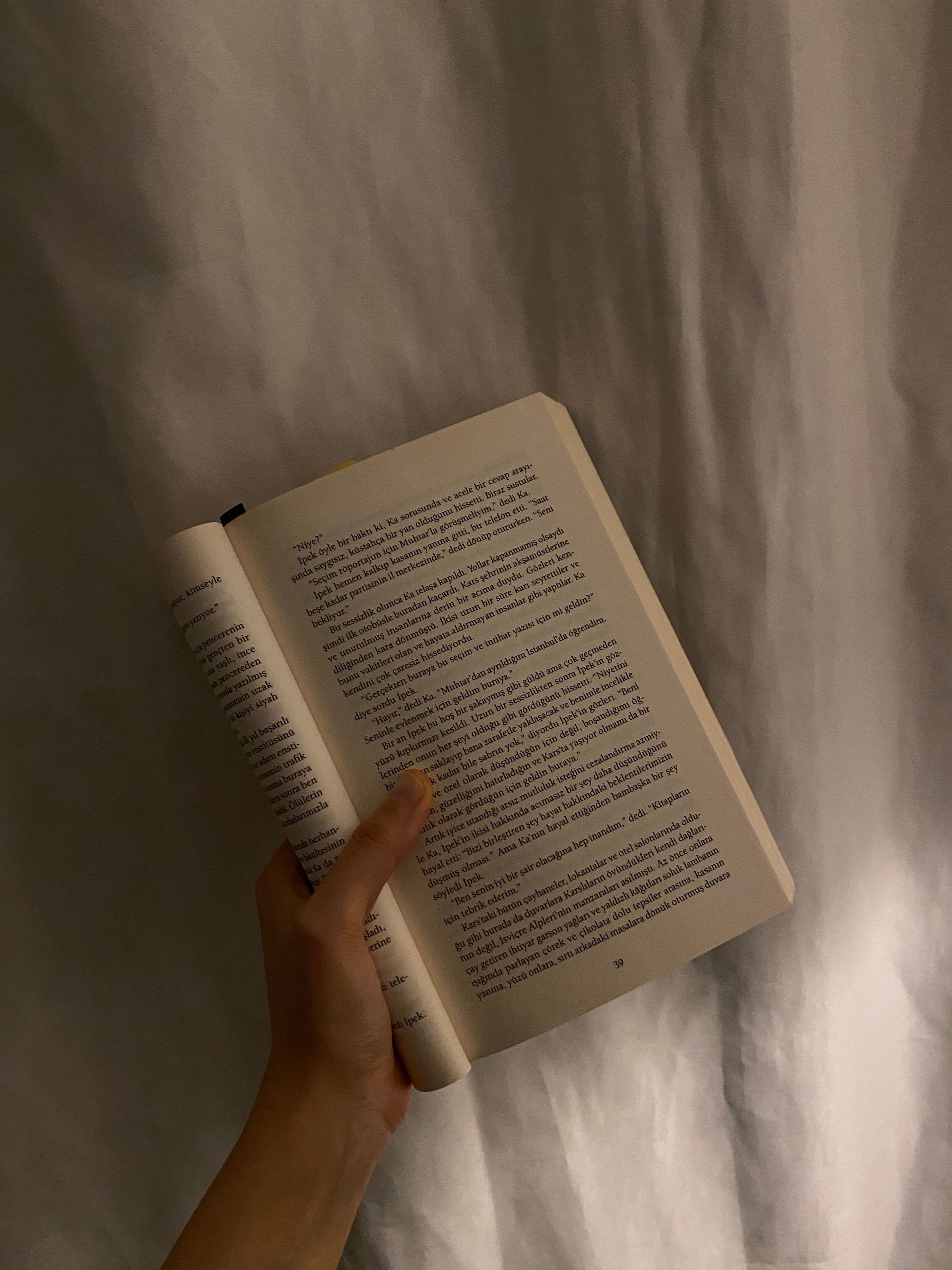 A lamp lit beside a book and a cup of tea on a bedside table