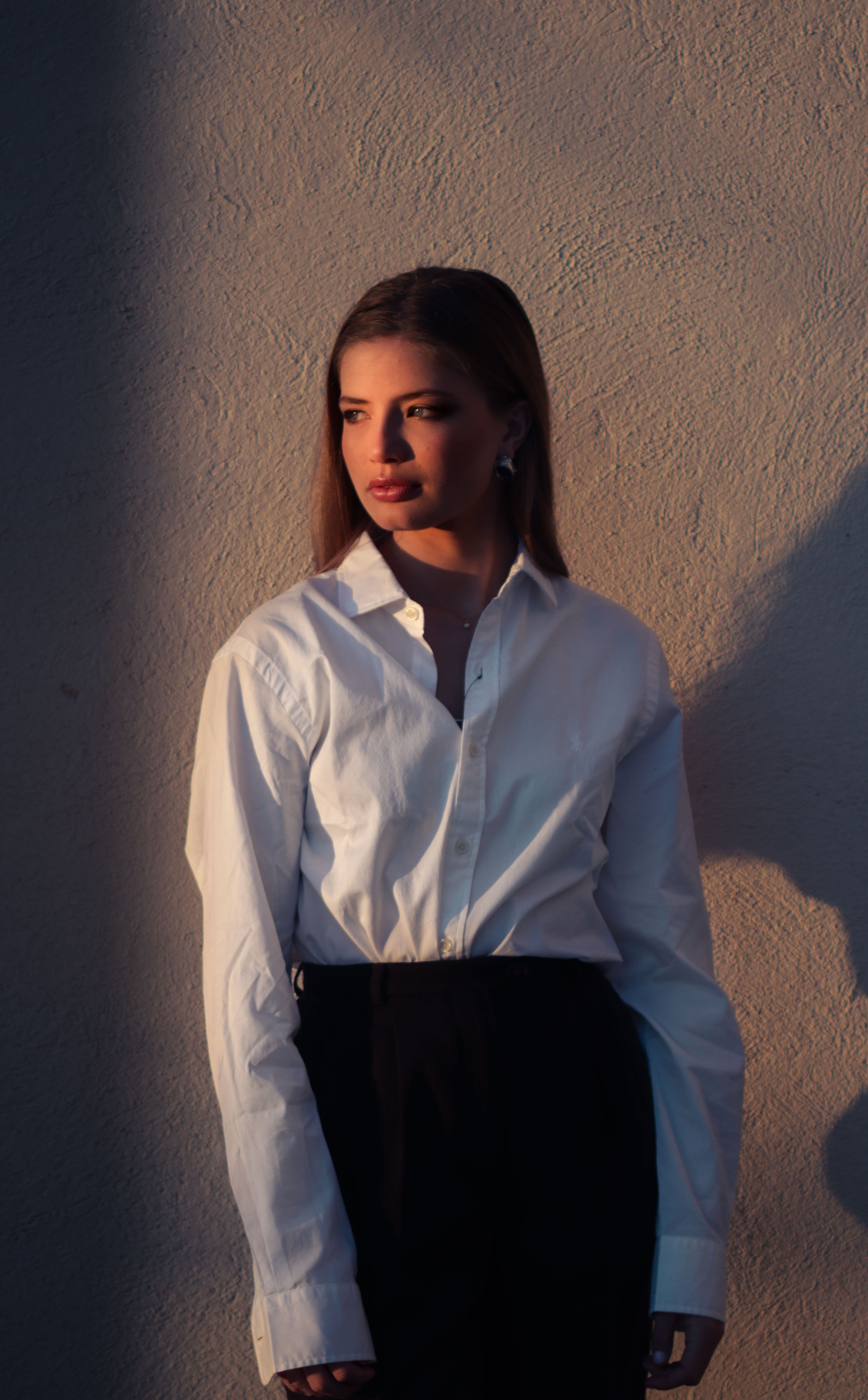 A softly creased white cotton shirt hanging from a wooden peg in morning light